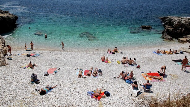 Una playa de guijarros con gente tomando el sol y nadando.