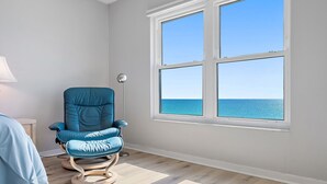 A room with a large window overlooking the sea, a blue chair, and a lamp. - GULF FRONT INDIAN ROCKS BEACH, REFLECTIONS VACATION CONDO (Indian Rocks Beach)