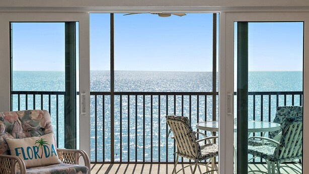 A balcony with a view of the ocean, featuring two wicker chairs and a small table. - GULF FRONT INDIAN ROCKS BEACH, REFLECTIONS VACATION CONDO (Indian Rocks Beach)