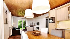 Een moderne keuken met houten kastjes, een eettafel met stoelen, een inbouwoven en een televisie aan de muur.