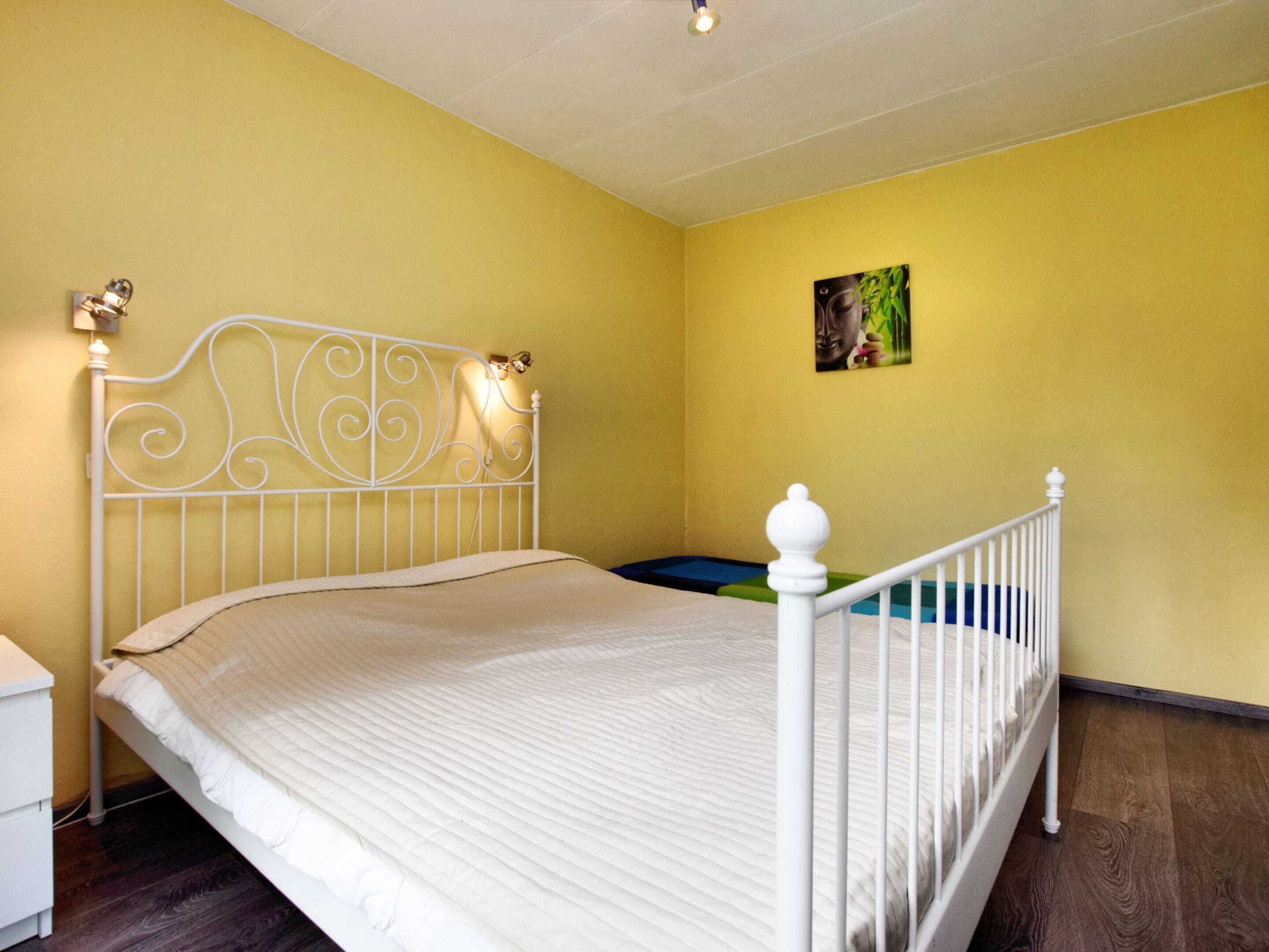 A single-bed room with a white metal headboard, a bedside table, and a small bedside lamp.