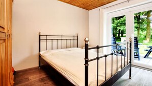 Een slaapkamer met een houten plafond, een metalen bed en uitzicht op een terras met stoelen en tafels.