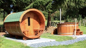 Een houten, vatvormig gebouw met een deur en ramen, een houten bankje en een sauna met banken.