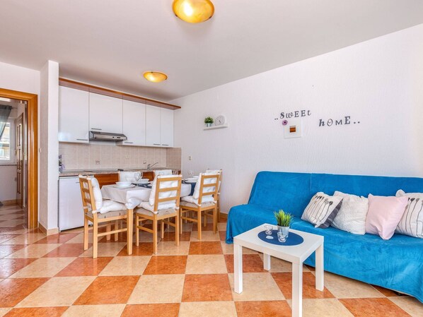 A compact living space with a dining area, kitchenette, and a blue sofa with cushions. - Modern Ground Floor Apartment With Private Terrace and Jacuzzi (Crikvenica)