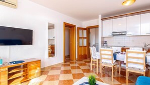 A modern living room with a flat-screen TV, wooden furniture, a dining area with a table and chairs, and a kitchen with white cabinets. - Modern Ground Floor Apartment With Private Terrace and Jacuzzi (Crikvenica)
