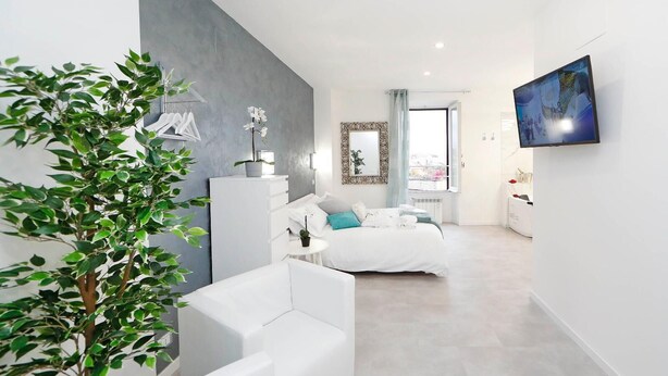 A modern bedroom with a bed, a white sofa, a small table, and a potted plant. - Trastevere Suite (Rome)