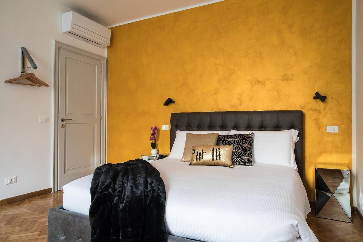 A bedroom with a large bed, a bedside table with a vase of flowers, and a wardrobe with a hanging rack.