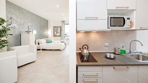 A modern, minimalist living room with a sofa, a coffee table, and a potted plant. The kitchen features white cabinets, a microwave, and a kettle on the counter. - Trastevere Suite (Rome)