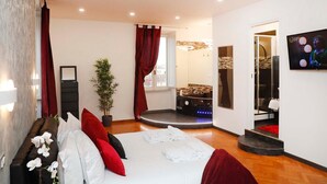 A modern hotel room with a large bed, a small bathroom with a bathtub, a potted plant, and a TV on the wall. - Trastevere Suite (Rome)