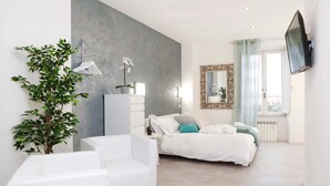 A modern bedroom with a bed, a white armchair, a large mirror, and a potted plant. - Trastevere Suite (Rome)