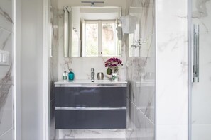 A modern bathroom with a marble floor, a large mirror, a sink with a dark cabinet, and a shower area. - Trastevere Suite (Rome)