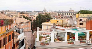 A high-rise building with multiple balconies, some with plants, and a view of the cityscape in the background. - Trastevere Suite (Rome)