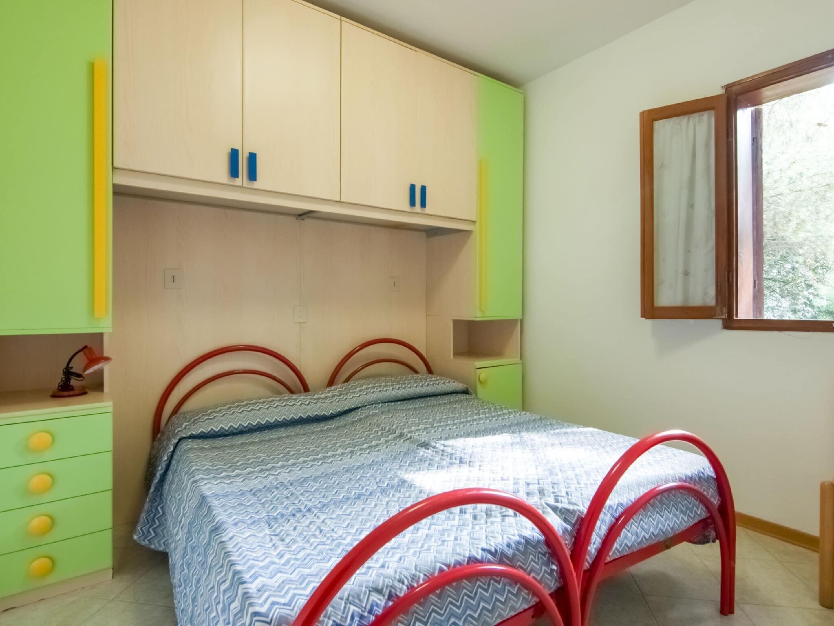 A bedroom with a bed, a desk, and a window.