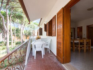 A balcony with a table and chairs, a wooden door, and a view of trees and buildings.