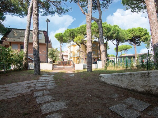 A paved pathway leading to a building complex with multiple trees and a clear sky.