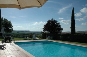 Ein Schwimmbecken mit Blick auf die Landschaft, umgeben von Liegestühlen und Sonnenschirmen.