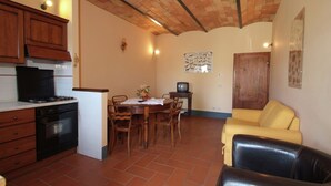 A kitchen with wooden cabinets, a stove, and a dining area with a table and chairs. - Peaceful Pienza Garden Escape (Pienza)