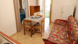 Ein kleiner, gut beleuchteter Raum mit Esstisch, zwei Stühlen, einer Couch und einer Tür, die auf einen Balkon führt.