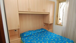 Ein kleines Zimmer mit einem Bett, Holzschränken und einem Fenster mit Vorhängen.