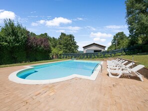 A rectangular swimming pool with a curved edge, surrounded by a brick deck. There are white lounge chairs aligned along the pool's edge.