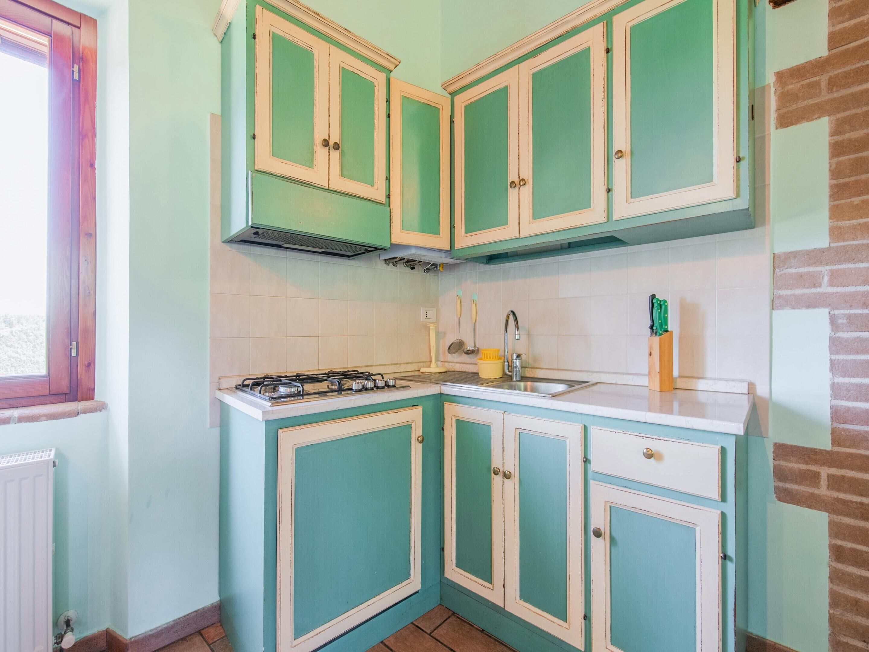 Een keuken met blauwgroene kastjes, een gasfornuis en een spoelbak.