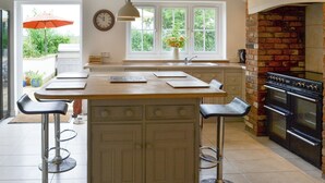 A kitchen with a central island, bar stools, a brick fireplace, and a window with a view of greenery. - 5 bedroom accommodation in Tilney St Lawrence, near Kings Lynn (Tilney St Lawrence, near Kings Lynn)