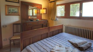 A bedroom with a wooden bed, a dresser with a mirror, a window with curtains, and a radiator. - Belvilla by OYO Olmi (Casole d'Elsa)