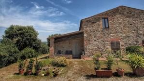 A stone building with a sloped roof, a covered porch, and potted plants in the foreground. - Belvilla by OYO Olmi (Casole d'Elsa)