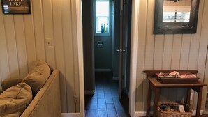 A hallway with wooden flooring, a sofa, a wicker basket, and a framed picture on the wall. - Raper’s Hollow Waterfront Cabin (Eucha)
