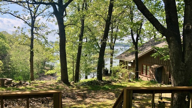 A cabin with a deck, surrounded by trees and a lake. - Raper’s Hollow Waterfront Cabin (Eucha)