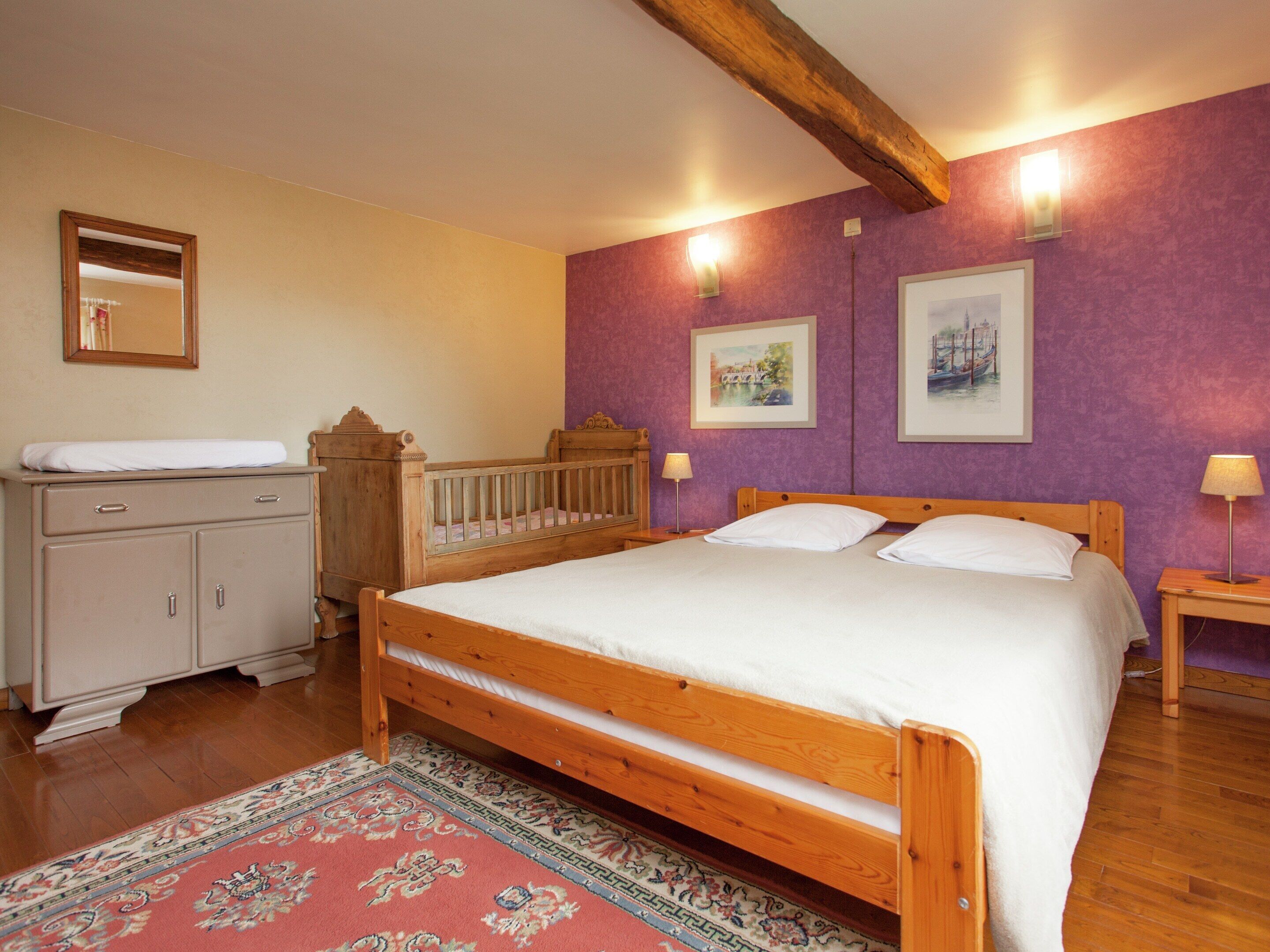 A bedroom with a wooden bed, a nightstand, a dresser, and two wall-mounted lamps.