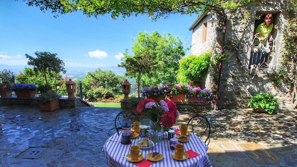 Un espace extérieur aménagé pour prendre les repas, avec une table dressée pour deux personnes, entouré de murs en pierre et de plantes en pot.