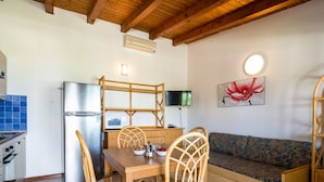 Una cocina compacta con refrigerador, microondas y estufa, una mesa de comedor con sillas, y un sofá con un cojín estampado.