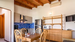 Cocina compacta con comedor, que incluye una mesa de madera, sillas de mimbre, un microondas y un estante empotrado para televisión.