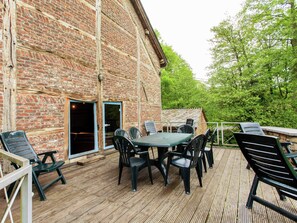 An outdoor patio with a brick building, a table with chairs, and a wooden deck. - Forest Escape, Luxembourg (Manhay)