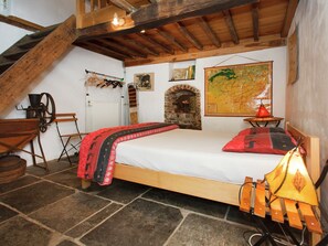 Une chambre avec un lit en bois, une cheminée en pierre, une carte accrochée au mur et une échelle en bois.