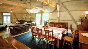 A rustic wooden interior with a dining area featuring a table with a checkered tablecloth, wooden chairs, and a chandelier. - Forest Escape, Luxembourg (Manhay)