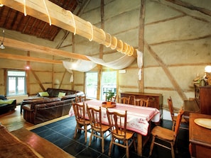 A rustic wooden interior with a dining area featuring a table with a checkered tablecloth, wooden chairs, and a chandelier.