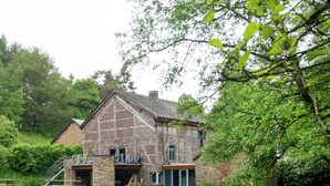 A stone building with a sloped roof, a staircase leading to a balcony, and a grassy lawn in front. - Forest Escape, Luxembourg (Manhay)