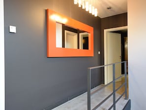 A hallway with a dark gray wall, a bright orange-framed mirror, and a metal railing.