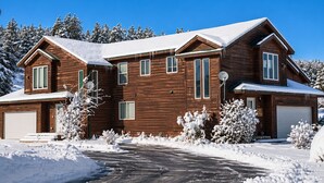 Una casa de madera de dos pisos con garaje, rodeada de árboles cubiertos de nieve.