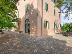A building with a stone-paved courtyard, green shutters, and outdoor seating.