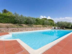 A rectangular swimming pool with a stone wall and tiled deck.