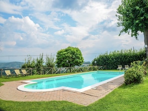 Una piscina rettangolare con bordo in mattoni, circondata da un'area verdeggiante e una recinzione in legno.