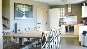 A dining area with a wooden table and chairs, a kitchen with white cabinets and appliances, and a painting on the wall. - Forest Cottage, Jehonville (Bertrix)