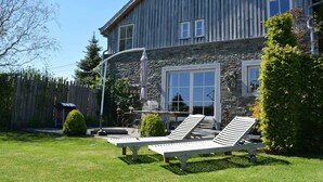 A large house with a stone facade, a covered patio, and two lounge chairs in the front yard. - Forest Cottage, Jehonville (Bertrix)