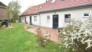 A white house with a red-tiled roof, a front door, and a small garden area with a patio. - Schone Ferienwohnung in Stellshagen mit Garten (Damshagen)