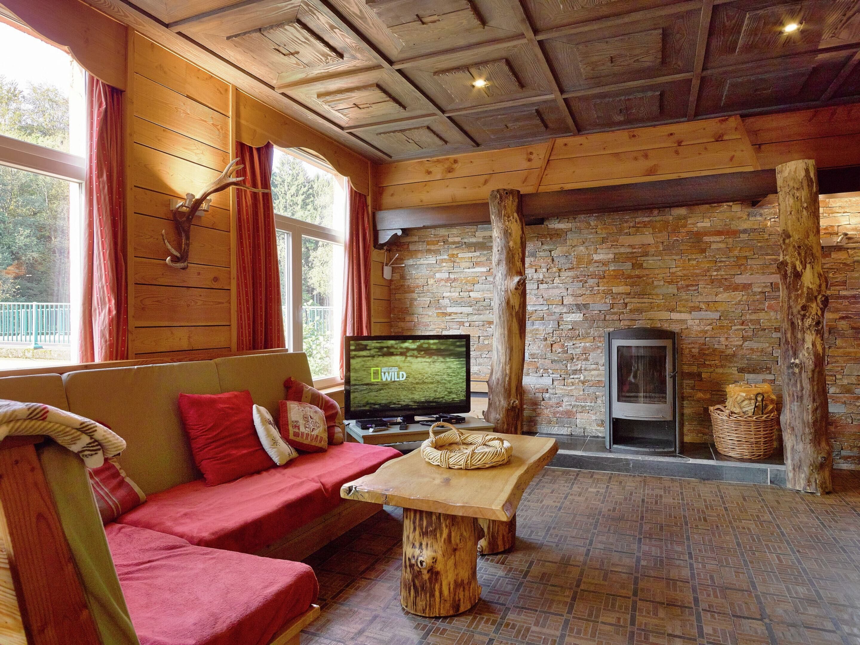 A cozy cabin interior with a wooden ceiling, a stone wall, a fireplace, and a television on a wooden table.