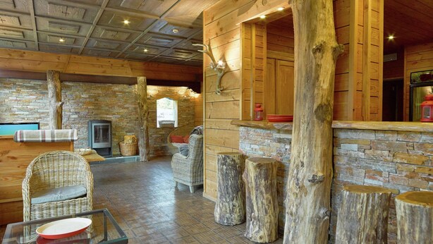 A rustic interior with a stone fireplace, wooden walls, and a glass table with a red plate. - Luxurious Villa in Stoumont With Sauna (Stoumont)