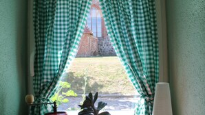 A window with green and white checkered curtains, a view of a brick building, and a small plant on the windowsill. - Apartment in Ribnitz Damgarten (Ribnitz-Damgarten)